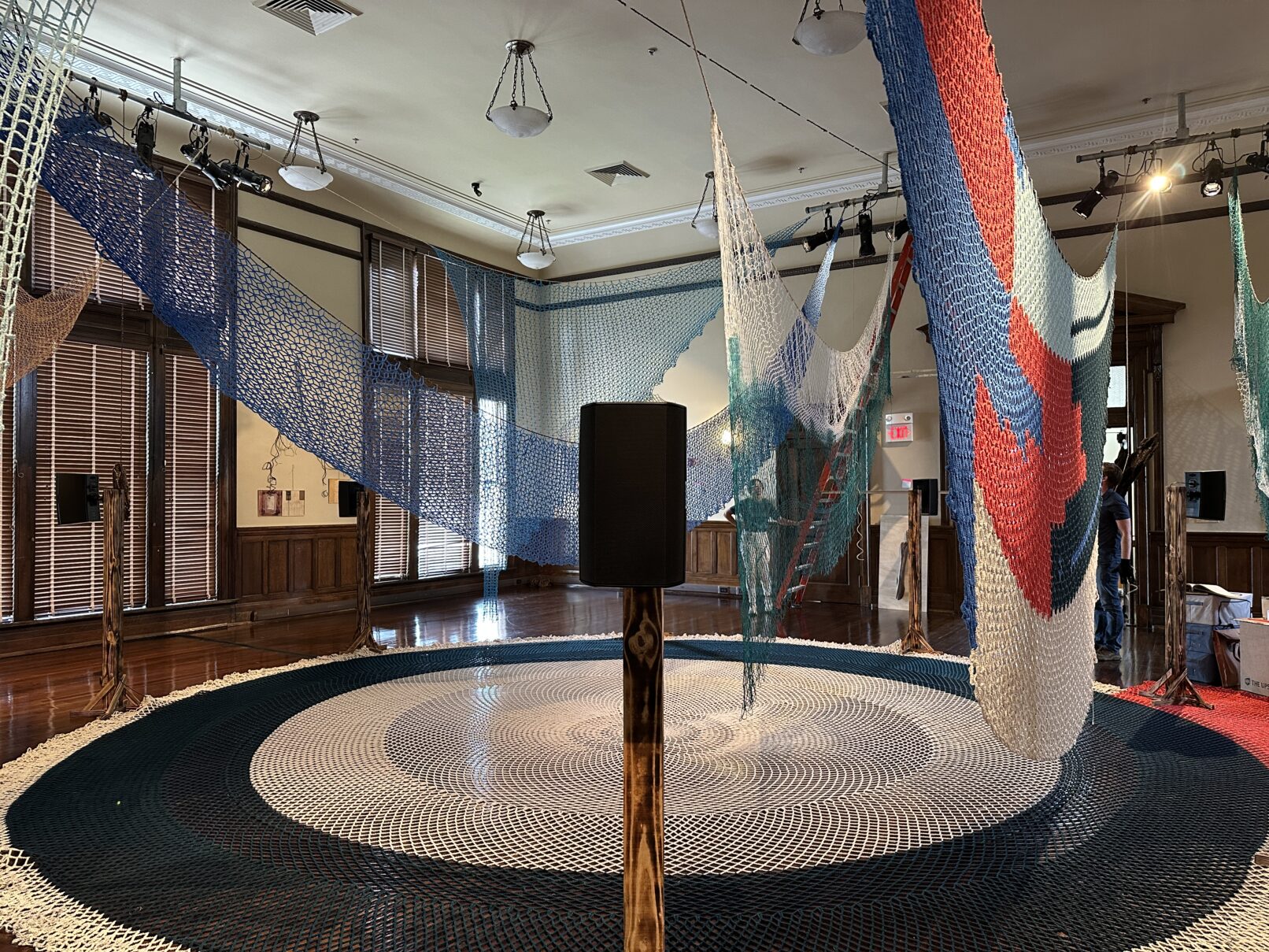 Gallery view of sound installation designed in collaboration with Porche Advanced Systems, LLC, Flare, 2025 (on floor), and other woven and crochet nets constructed by Jessica McMahon, Pattie Toenies, Jeri Grotberg, Janice Salminen, and Victoria Bradford Styrbicki