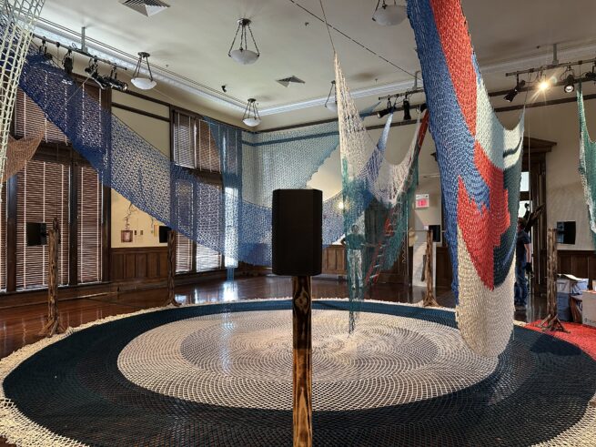 Gallery view of sound installation designed in collaboration with Porche Advanced Systems, LLC, Flare, 2025 (on floor), and other woven and crochet nets constructed by Jessica McMahon, Pattie Toenies, Jeri Grotberg, Janice Salminen, and Victoria Bradford Styrbicki