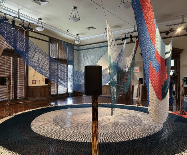 Gallery view of sound installation designed in collaboration with Porche Advanced Systems, LLC, Flare, 2025 (on floor), and other woven and crochet nets constructed by Jessica McMahon, Pattie Toenies, Jeri Grotberg, Janice Salminen, and Victoria Bradford Styrbicki